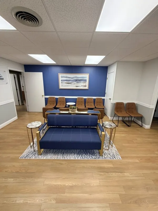 Modern waiting area featuring blue cushioned chairs on a patterned rug, light wood flooring, blue accent wall, and contemporary decor.