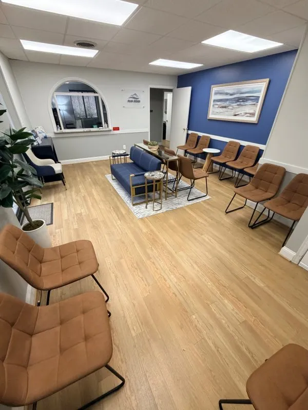 Bright waiting room with light wood flooring, brown cushioned chairs, blue accent wall with framed artwork, and natural lighting.